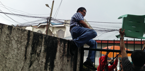 Picture shows Dr Aris Alip climbing over a fence to reach a CARD MRI branch in Ormoc City as he joins the search team to personally visit members and staff in the affected areas. Copyright ICMIF