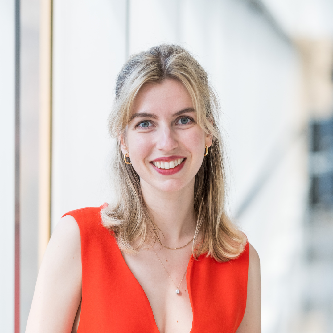 Barbora Kotoun, a blonde woman looking ahead and smiling wearing an orange dress. 