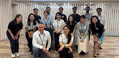Group photo of several people standing and kneeling together in an indoor space with a sign in the background that reads ‘Metro Innovation Garden.