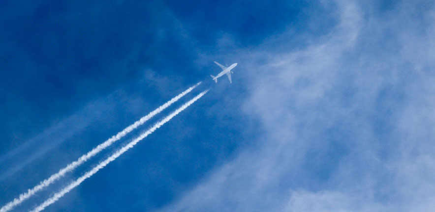A white airplane flying high in a blue sky, leaving two long white contrails behind it as it moves through thin, wispy clouds.