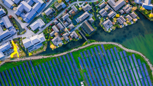Aerial view of a modern residential area with waterways beside a large field of blue solar panels set on green land.