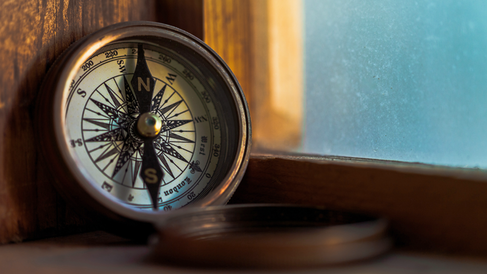 Close-up of a brass compass resting on wood, lit by warm sunlight near a window.