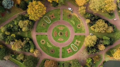 Aerial view of a circular landscaped garden with concentric pathways, flower beds, and surrounding trees, illustrating circular design and resource flow principles.