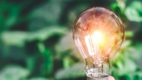 Illuminated light bulb held against a blurred green background, symbolising energy efficiency, innovation, and sustainable solutions.