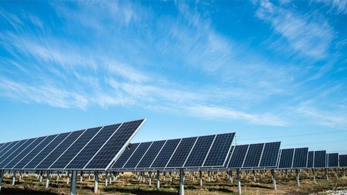 Rows of solar photovoltaic panels installed in an open field beneath a blue sky, generating renewable electricity from sunlight.