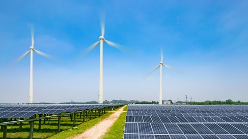 Large-scale solar farm with photovoltaic panels and wind turbines producing renewable electricity in a rural landscape.