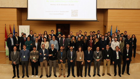 Group photo of approximately 70 conference attendees standing on a stage in a large wood-panelled auditorium beneath a projection screen displaying a Spanish-language presentation slide.