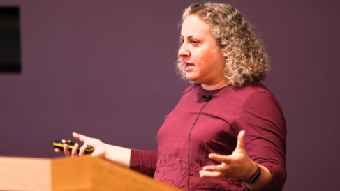 A woman stood in front of a lecturn with hand outreached to her sides