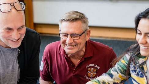 Three students looking at a laptop screen off camera and smiling