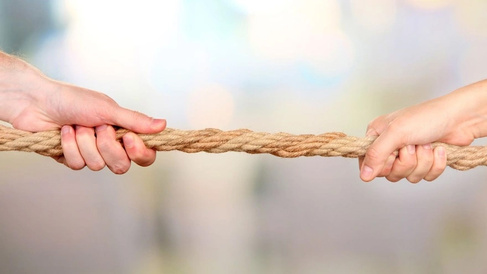 Two hands grip opposite ends of a thick twisted rope, pulling against each other in a tense tug‑of‑war.