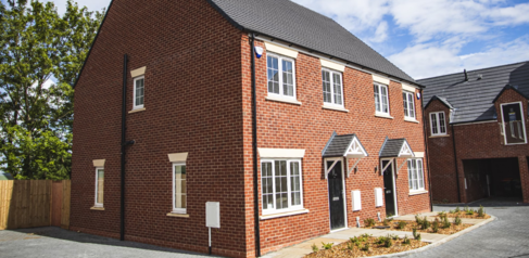 Image of a red brick semi detached new build house with coach house style houses behind