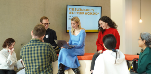 Seven students sat and stood in a circle working on a presentation