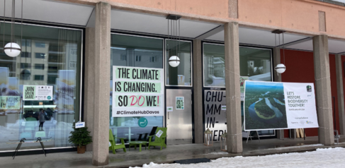 Image of a building with three large glass windows with posters stuck to the windows
