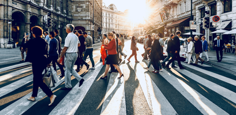 People crossing a zebra crossing on a busy street with the sun setting behind
