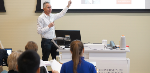 A man with his hand in the air presenting to a group of students