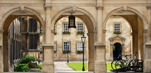 A photo of one of the Cambridge colleges with some arches, parked bicycles and a quad of grass in the background