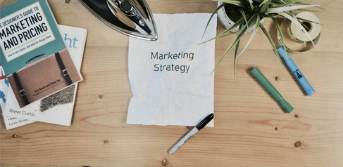 Desk with books, stationary and a notepad that reads 'marketing strategy'