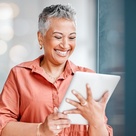 Mature woman with beautiful short, grey hair, smiling and reading from a tablet