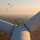 People standing on top of wind turbine, looking into a whole wind farm