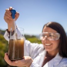 Woman in lab gear holding a pipette and probing water solution with soil