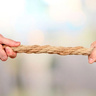 Two hands grip opposite ends of a thick twisted rope, pulling against each other in a tense tug‑of‑war.