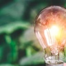 Illuminated light bulb held against a blurred green background, symbolising energy efficiency, innovation, and sustainable solutions.