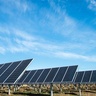 Rows of solar photovoltaic panels installed in an open field beneath a blue sky, generating renewable electricity from sunlight.