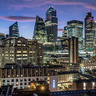 Twilight view of central London’s skyline, featuring The Gherkin, The Leadenhall Building, and other illuminated skyscrapers rising above older brick buildings under a blue‑purple dusk sky.