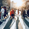People crossing a zebra crossing on a busy street with the sun setting behind