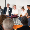 panel discussion with experts on tall chairs infront of audience.