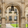 A photo of one of the Cambridge colleges with some arches, parked bicycles and a quad of grass in the background
