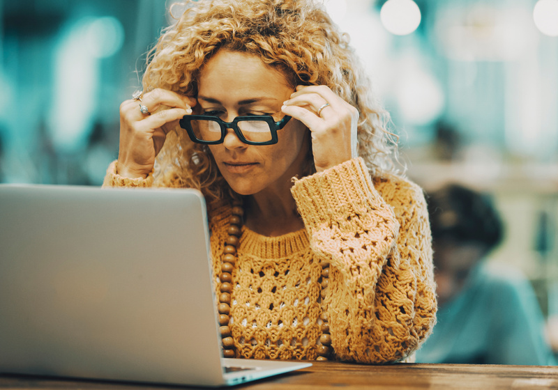 Woman holding her glasses, working at laptop.