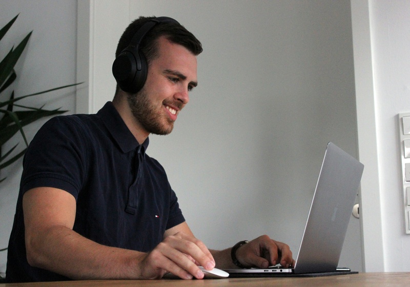 Man smilin, wearing headphones and using his laptop