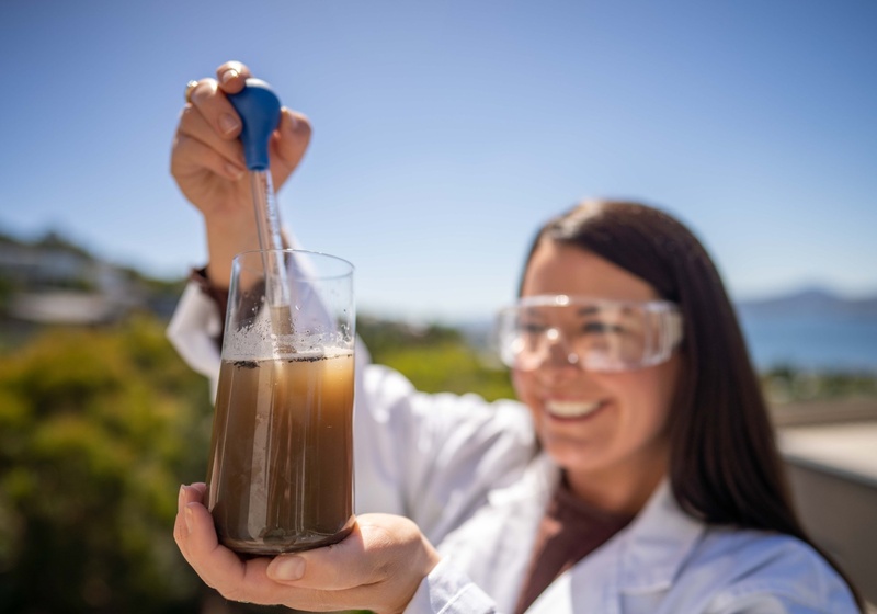Woman in lab gear holding a pipette and probing water solution with soil