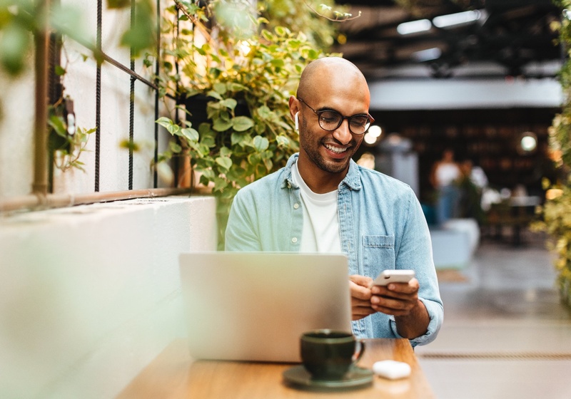 Smiling man working at modern office in front of laptop and using his phone and headphones.