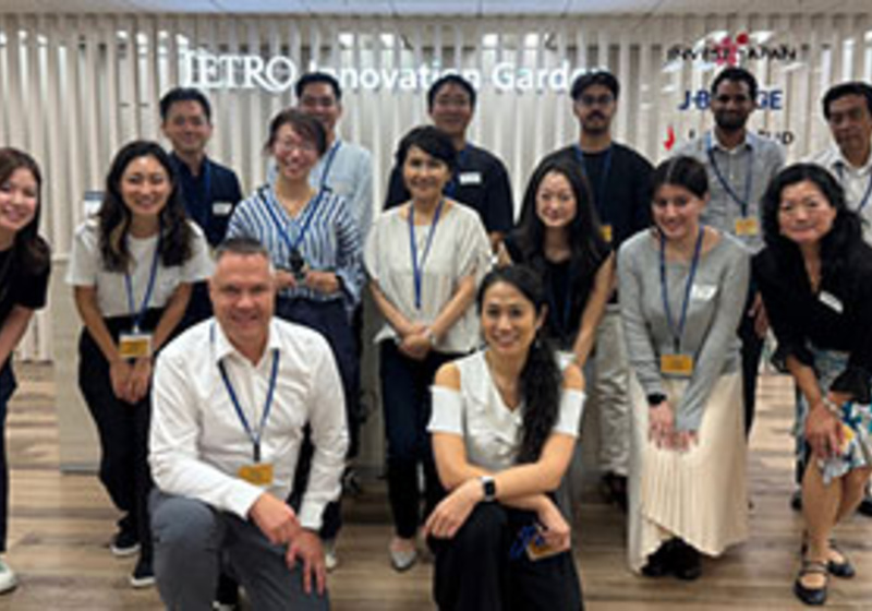 Group photo of several people standing and kneeling together in an indoor space with a sign in the background that reads ‘Metro Innovation Garden.