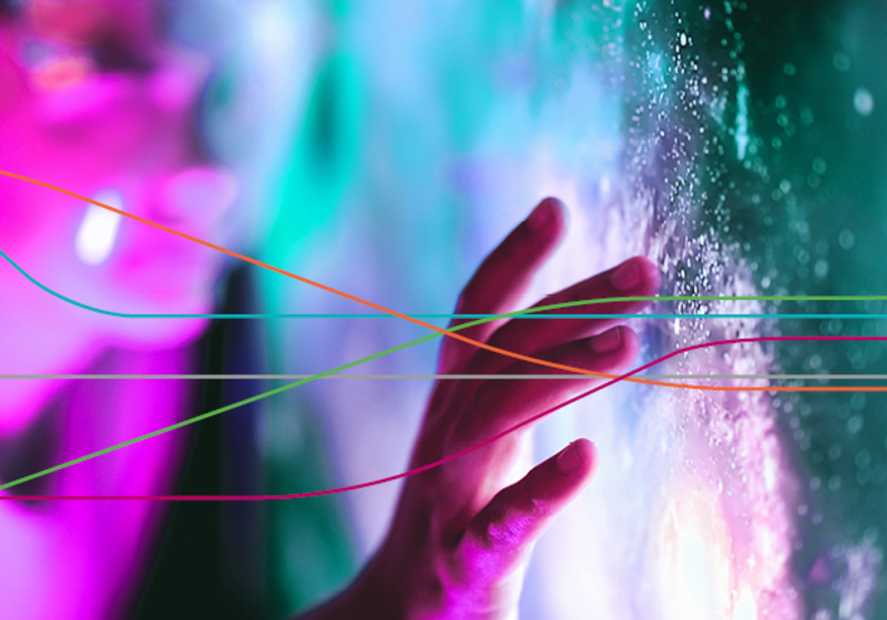 Close-up of a hand touching a brightly lit, textured surface with glowing pink and teal lights in the background, overlaid by several thin, multicoloured curved lines.