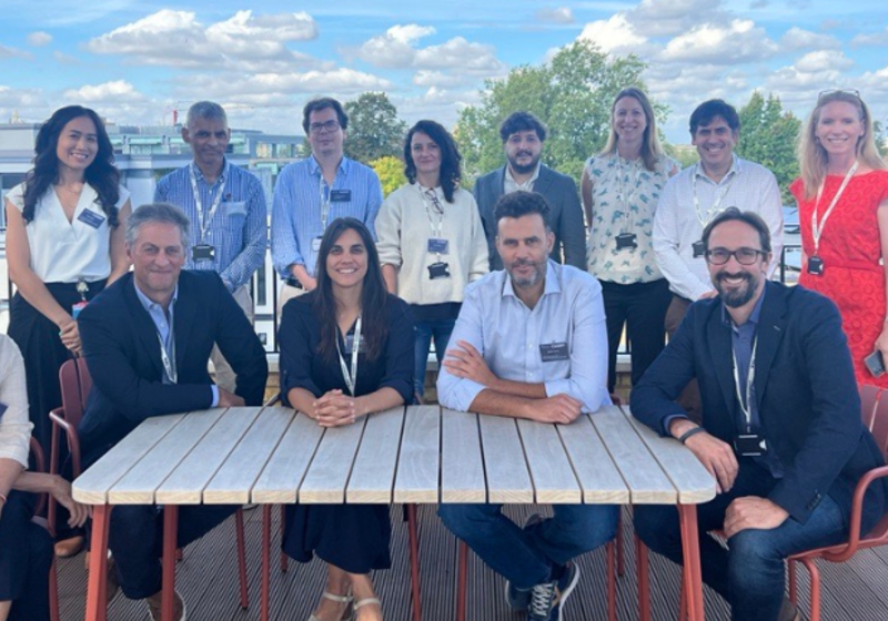 A group photo of spanish starups and innovators on a roof top terrace at Entopia in Cambridge smiling at the camera with blue skies and sunshine around them. 