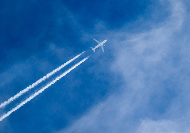 A white airplane flying high in a blue sky, leaving two long white contrails behind it as it moves through thin, wispy clouds.