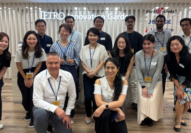 A cohort of smiling Japanses innovators gather together to take a group photograph in the X Hub building in Tokyo. 