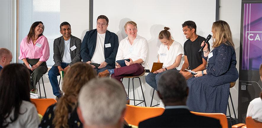 Living Lab panel discussion with experts on tall chairs infront of audience.