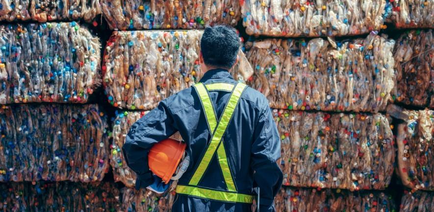 Worker standing in front of bales of plastic. Photo by Adobe Stock